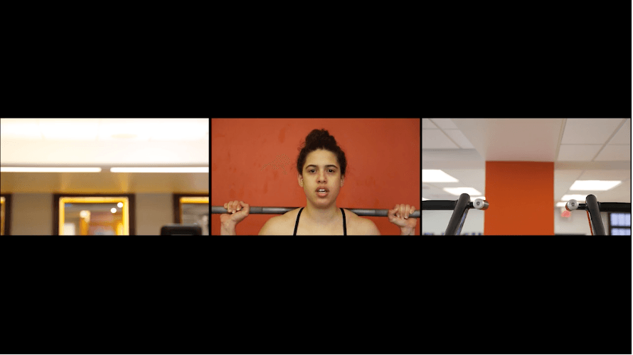 A woman exercises against an orange background in a video still.